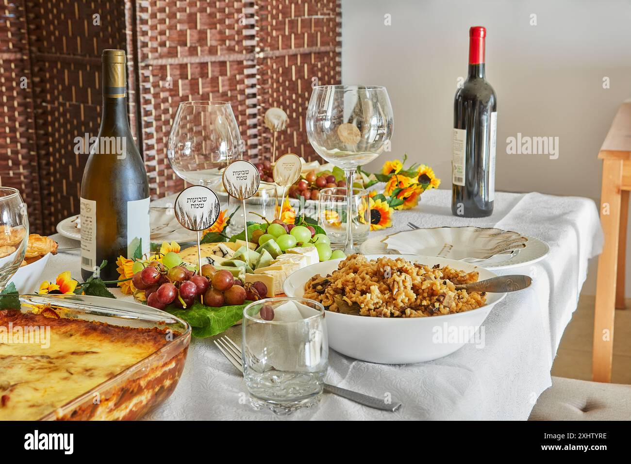 Ein eleganter Shavuot-Feiertagstisch mit Wein, Käse, Obst und Weihnachtsdekoration, bereit für ein traditionelles jüdisches Feiertagsessen. Happy Shavuot Inscript Stockfoto
