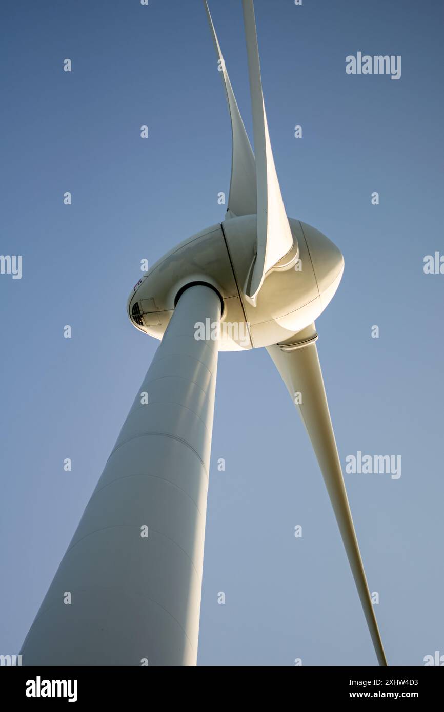 Dieses Bild zeigt eine Nahaufnahme einer modernen Windturbine mit niedrigem Winkel vor einem klaren blauen Himmel. Das schlanke, aerodynamische Design des b Stockfoto