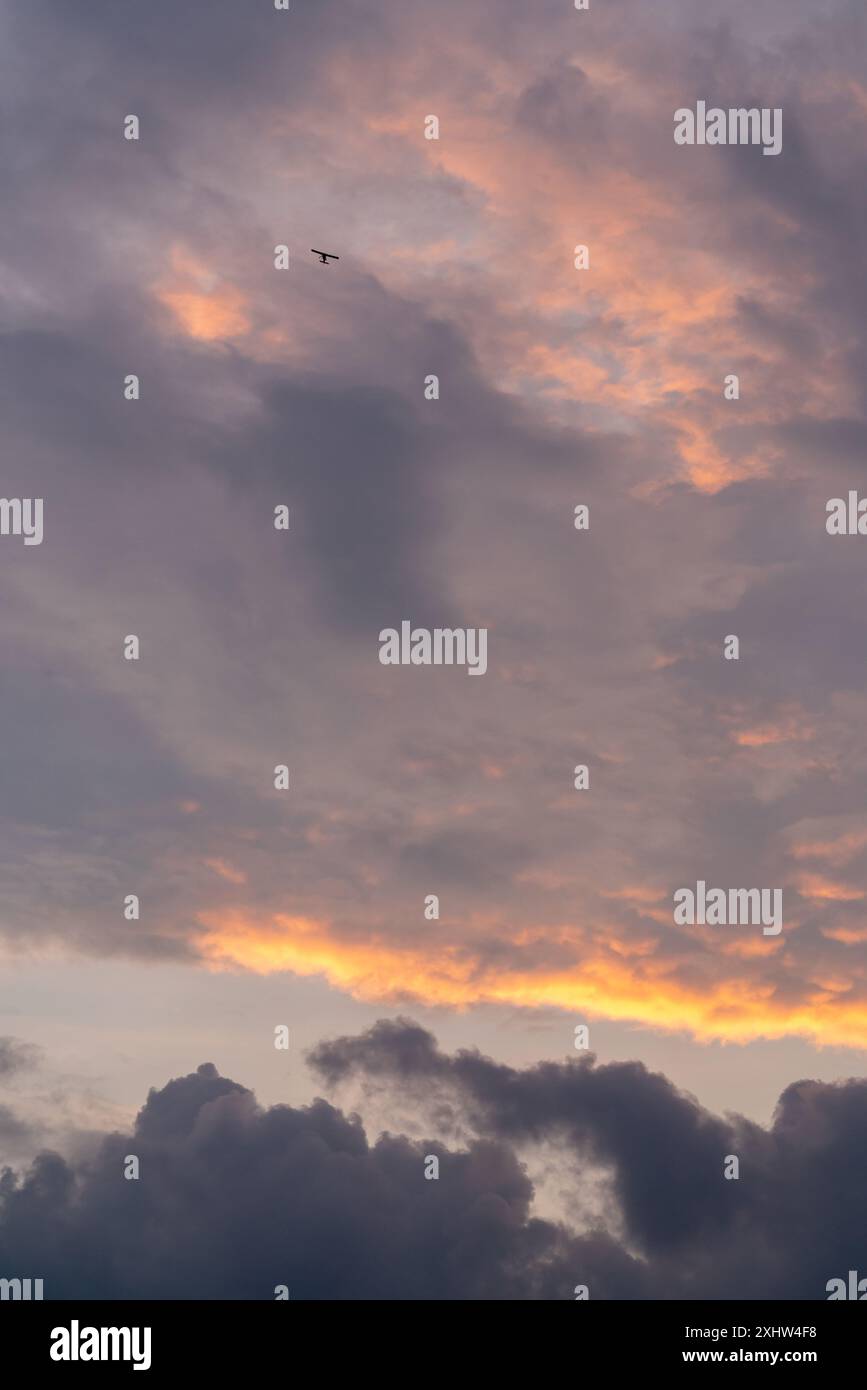 Wunderschöner Sonnenuntergangshimmel. Wolken bei Sonnenuntergang. Ein kleines Flugzeug fliegt am dunklen Himmel Stockfoto