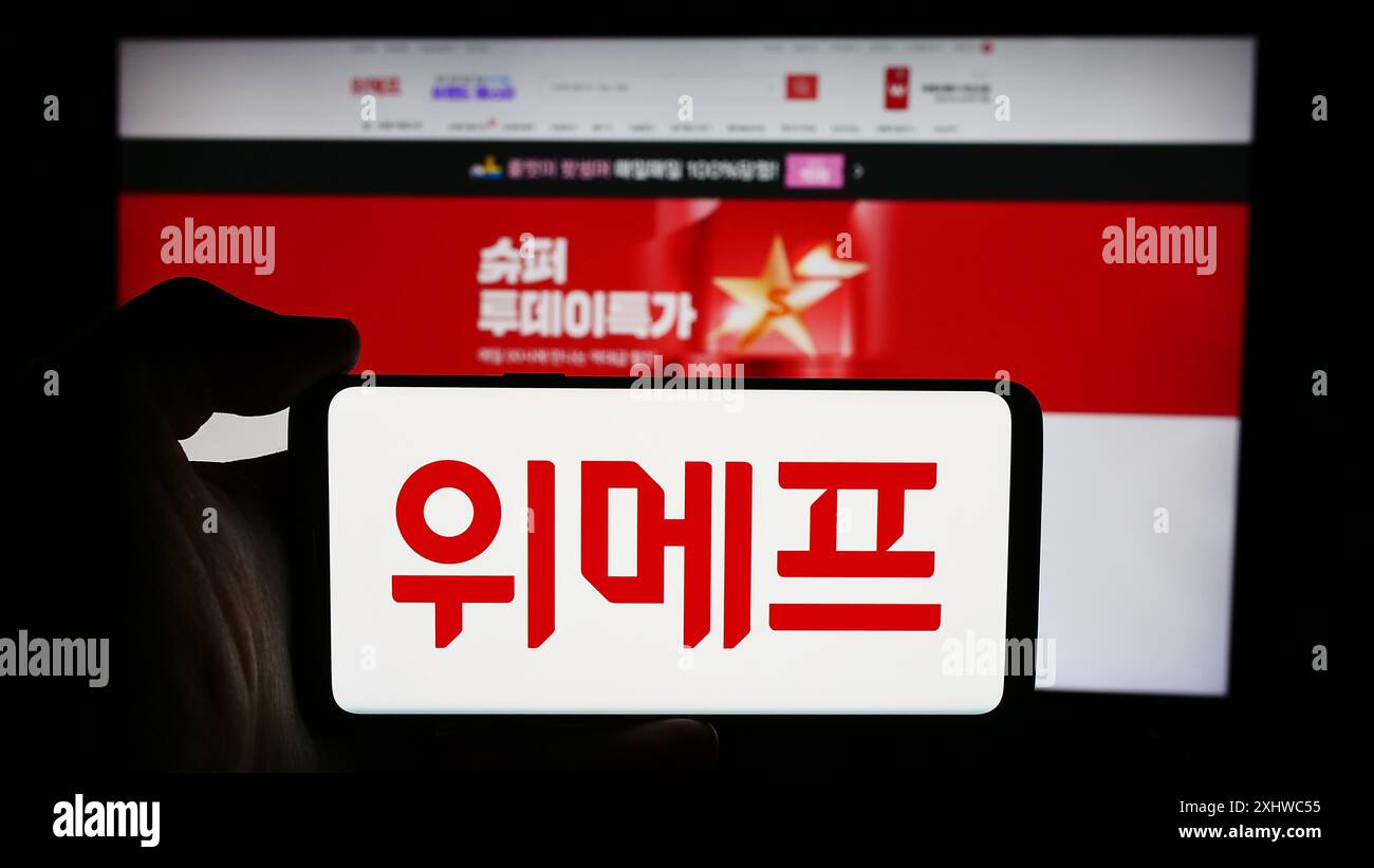 Person, die ein Mobiltelefon mit dem Logo des südkoreanischen E-Commerce-Unternehmens Wemakeprice vor der Business-Website hält. Schwerpunkt auf dem Display des Telefons. Stockfoto