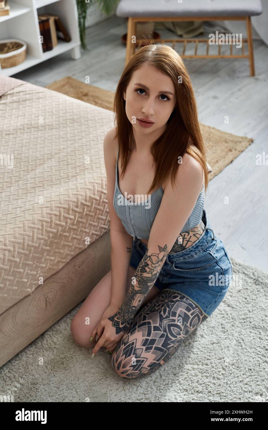 Eine junge Frau mit Tattoos sitzt auf dem Boden ihres modernen Apartments und genießt ein gemütliches Wochenende. Stockfoto