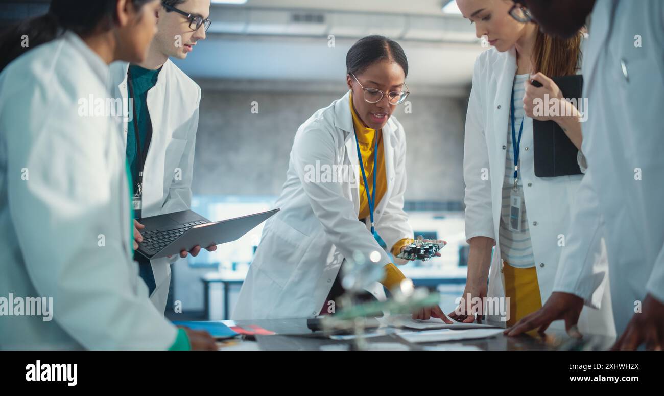 Gruppe junger professioneller Spezialisten, die Probleme mit Laptop- und Tablet-Computern zusammenstellen und lösen. Manufacturing Project Manager diskutieren Blueprint, in der Produktanalyse erfasste Daten. Stockfoto