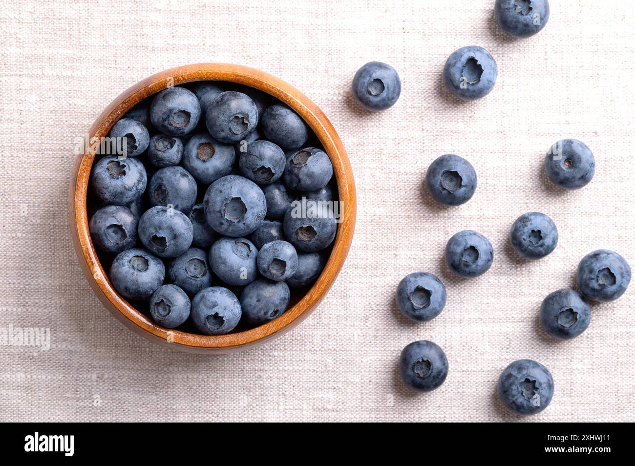 Heidelbeeren in einer Holzschale auf Leinenstoff. Dunkelblaue, reife, rohe Beeren, Früchte von Vaccinium corymbosum, angebaute Heidelbeeren. Stockfoto