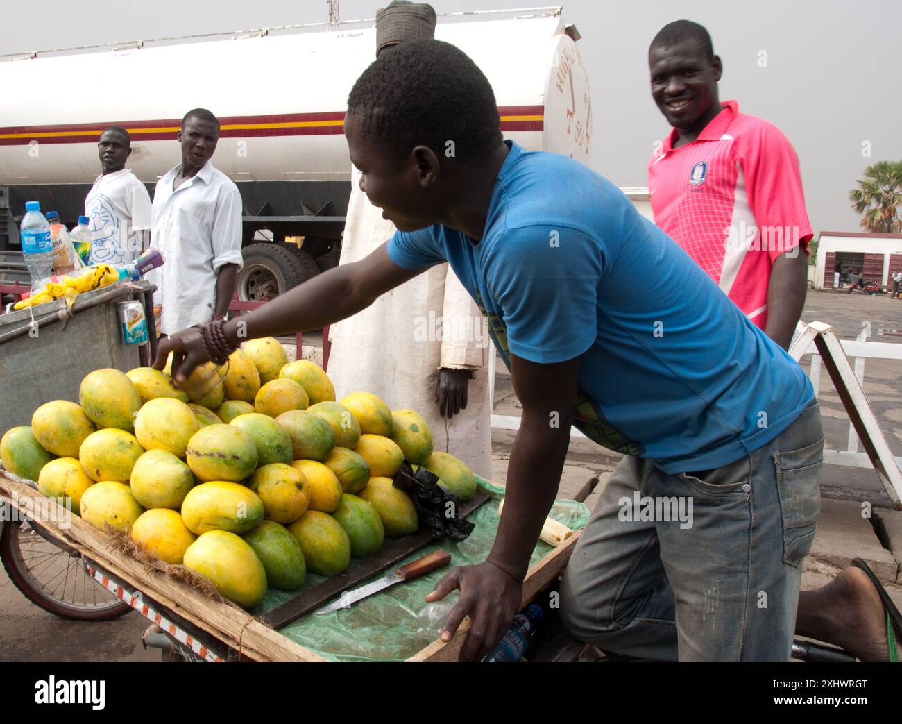 Mangostand, Bauchi, Bauchi, Nigeria, Afrika. Junge Mn, die Mangos aus einem kleinen Wagen vor einer Tankstelle verkauft, mit Tankwagen im Stockfoto