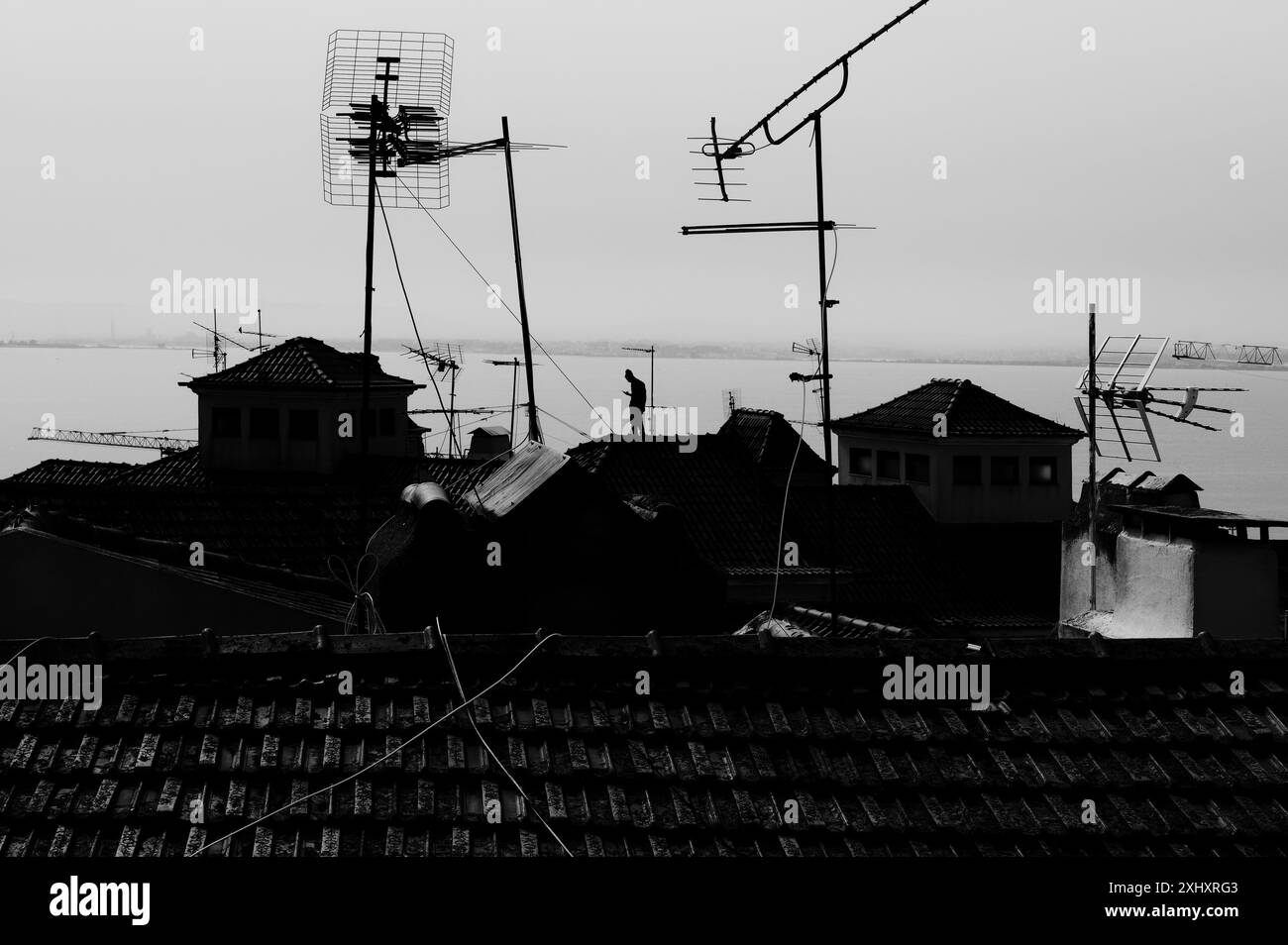 Monochrom eines Mannes, der auf den gekachelten Dächern in Alfama steht und den Fluss Tejo überblickt Stockfoto
