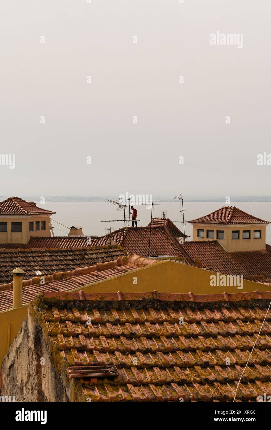 Ein Mann steht auf den rot gekachelten Dächern in Alfama mit Blick auf den Tejo Stockfoto