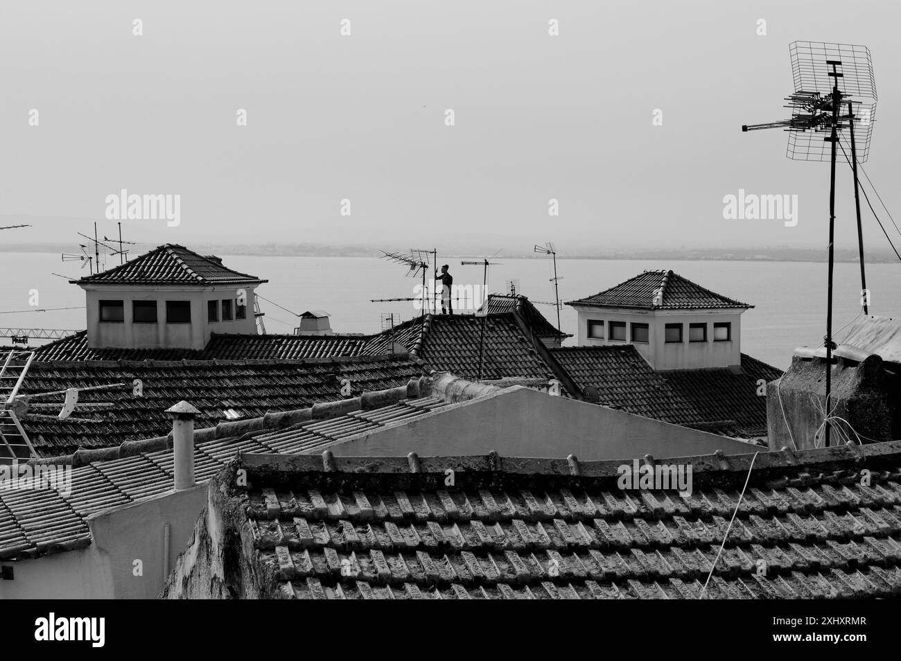 Ein Mann steht auf den rot gekachelten Dächern in Alfama mit Blick auf den Tejo Stockfoto