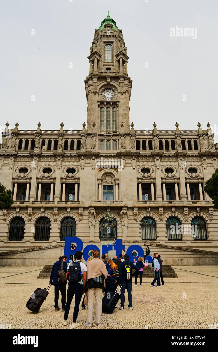 Touristen mit Gepäck stehen an einem bewölkten Tag vor den blauen Buchstaben im Câmara Municipal do Porto an Stockfoto