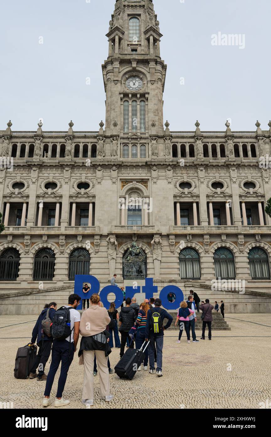 Touristen mit Gepäck stehen an einem bewölkten Tag vor den blauen Buchstaben im Câmara Municipal do Porto an Stockfoto