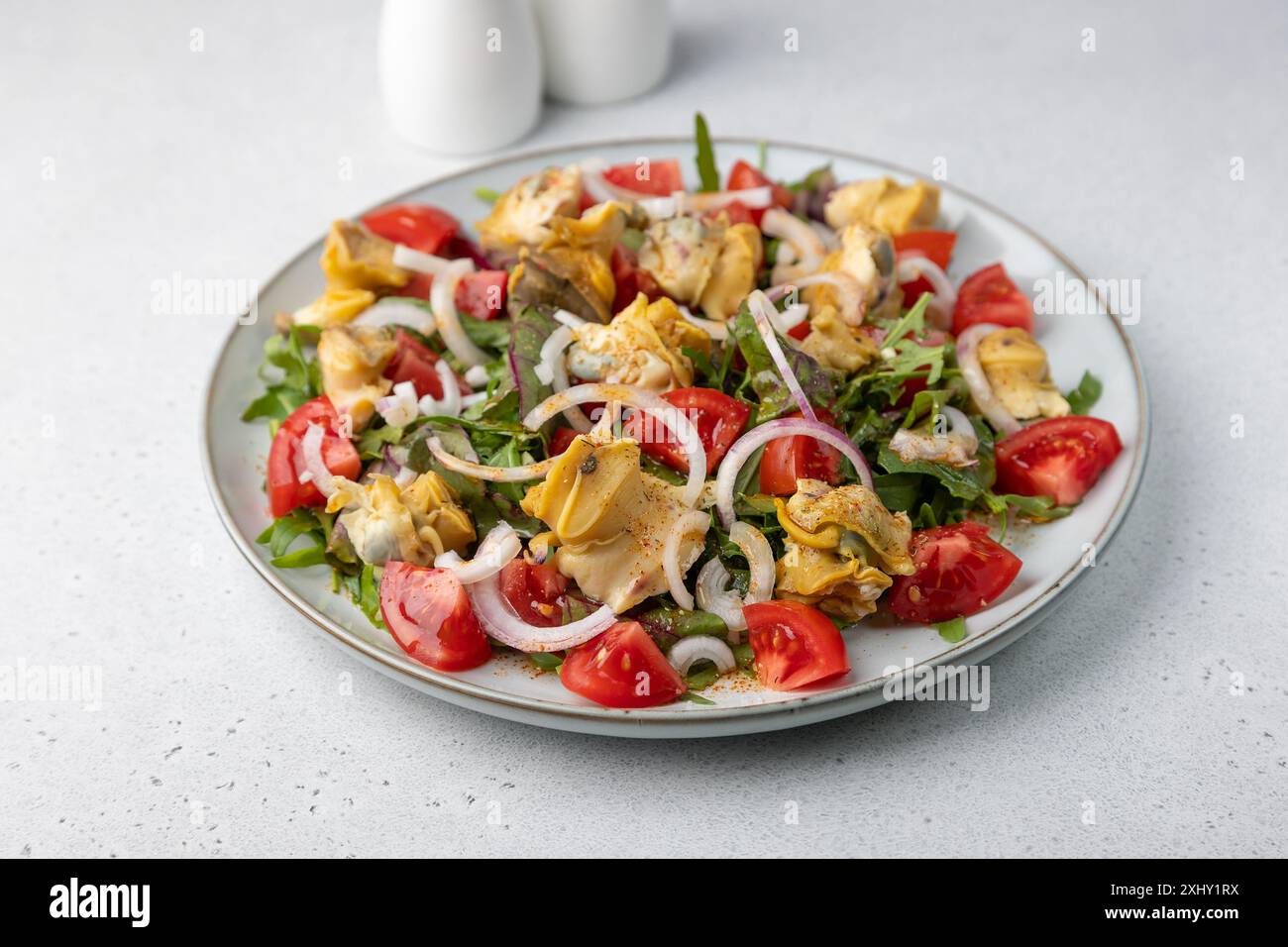 Warmer Salat mit rapan (Schnecken), Tomaten, Zwiebeln, Blattgemüse und Olivenöl. Traditioneller Salat mit Meeresfrüchten. Nahaufnahme, selektiver Fokus. Stockfoto