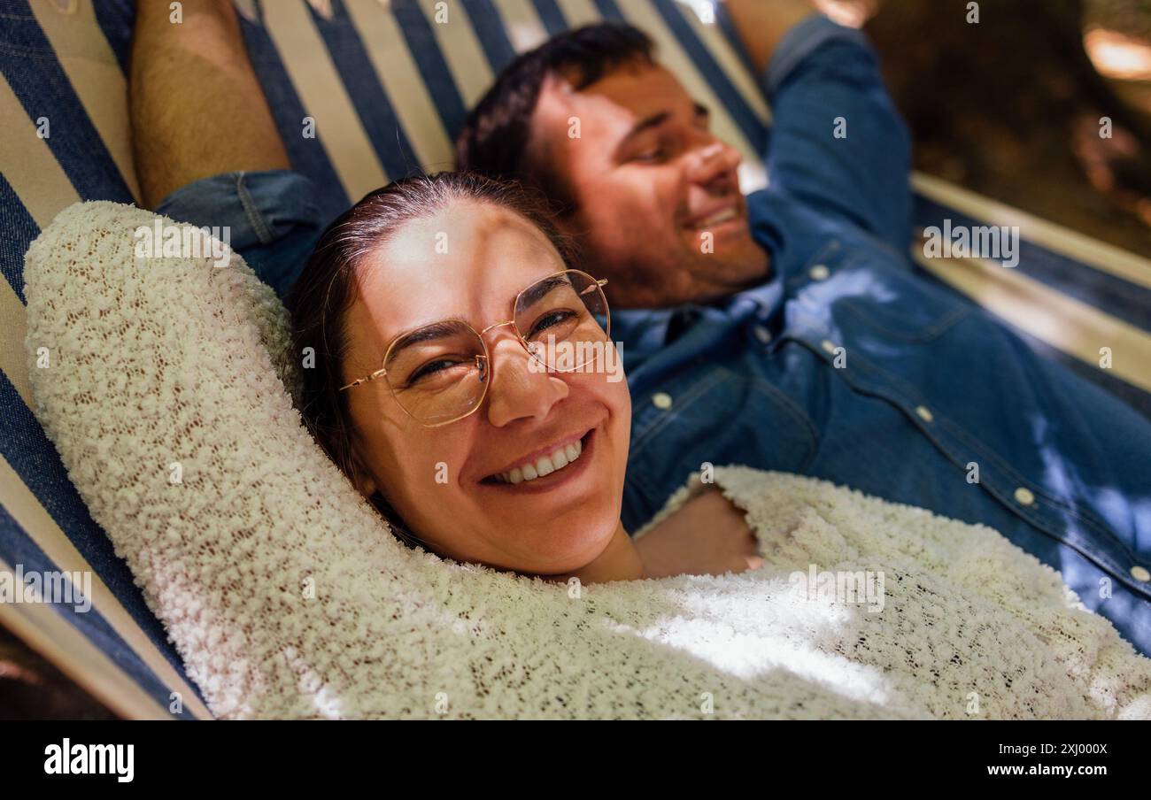 Ein junges verheiratetes Paar entspannt sich im Hinterhof des Hauses. Ein attraktiver Ehemann und eine Frau liegen draußen in einer Hängematte. Eine glückliche Familie gibt aus Stockfoto