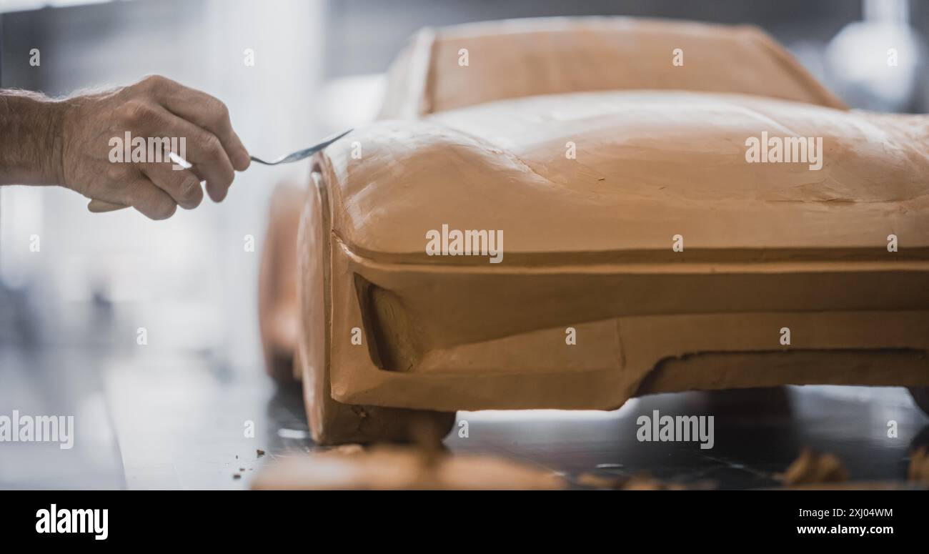 Nahaufnahme eines spezialisierten Modellierers, der am ersten Schritt der Fahrzeugproduktion arbeitet und ein 3D-Fahrzeugmodell im Miniaturmaßstab aus Lehm erstellt. Anonymer Mann, der die Oberfläche eines Konzeptfahrzeugs sorgfältig trimmt Stockfoto