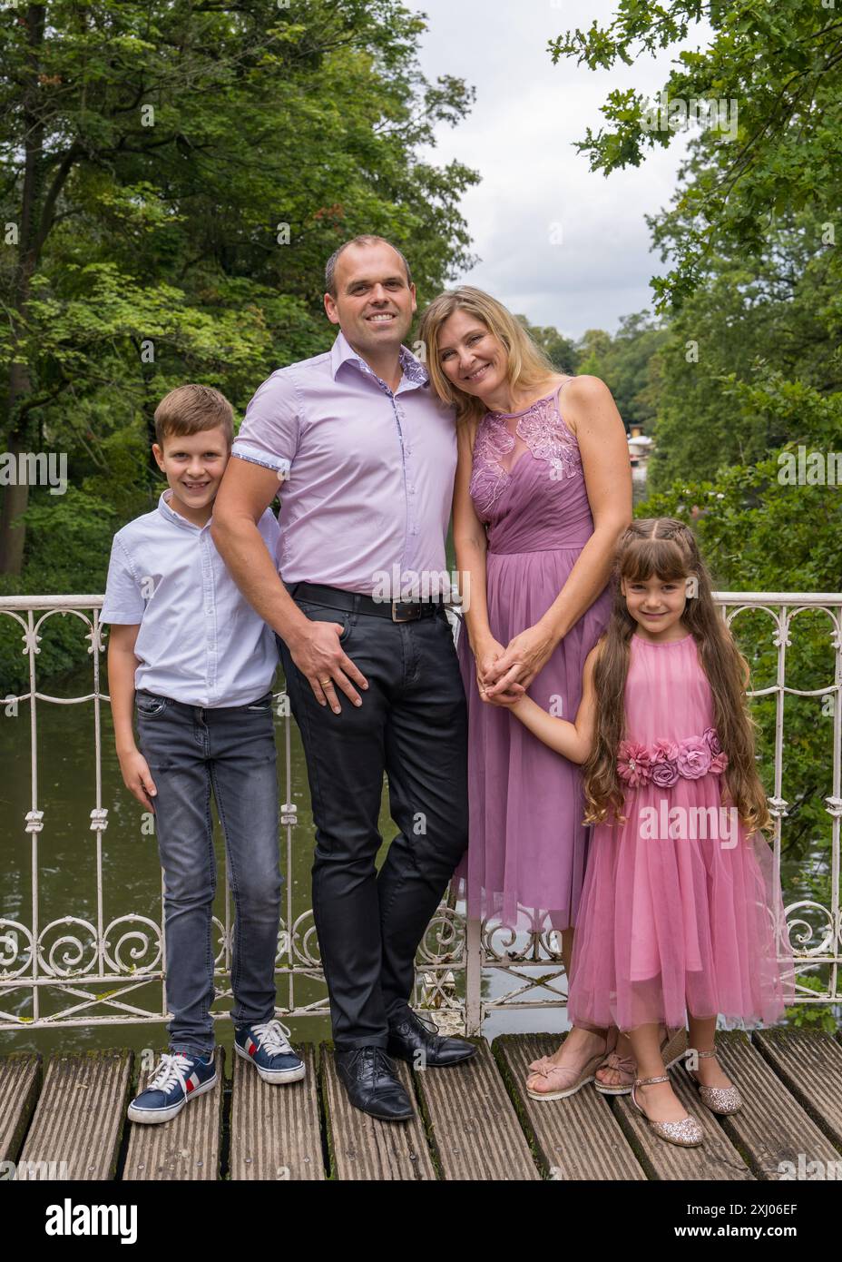 Porträt einer glücklichen Familie. Lachende Papa und Mom, Teenager-Sohn und kleine Tochter stehen auf einer weißen Brücke im Park. Mom und Mädchen sind in bea gekleidet Stockfoto