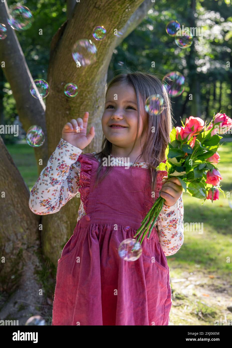 Nahaufnahme Porträt eines kleinen süßen Mädchens. Ein Kind hält einen kleinen Rosenstrauß. Seifenblasen fliegen in der Nähe. Freude, Freude, glückliche Kindheit Stockfoto