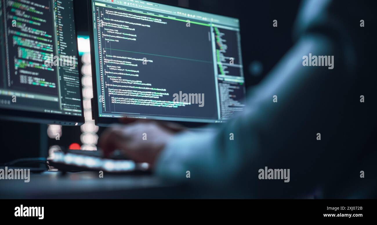 Nahaufnahme von schwarzen männlichen Händen, die auf einer Desktop-Computertastatur im Dark Network Security Office tippen. Professioneller Programmierer, der Code schreibt, wird auf zwei Monitorbildschirmen angezeigt. High-Tech-Entwicklungskonzept. Stockfoto