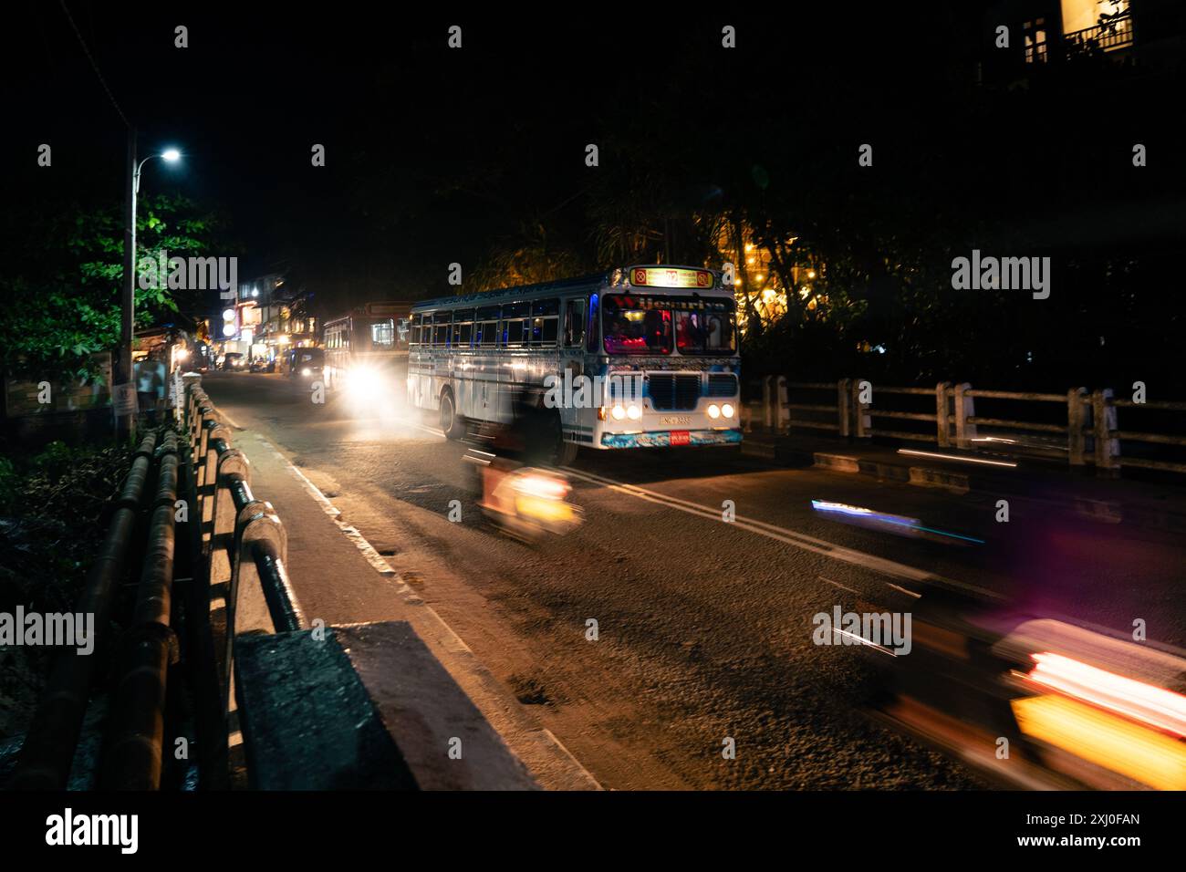 Ein hell beleuchteter Bus fährt nachts schnell auf einer Straße entlang. Der Bus ist mit farbenfrohen Lichtern dekoriert, und seine Scheinwerfer beleuchten die Straße vor Ihnen. Stockfoto