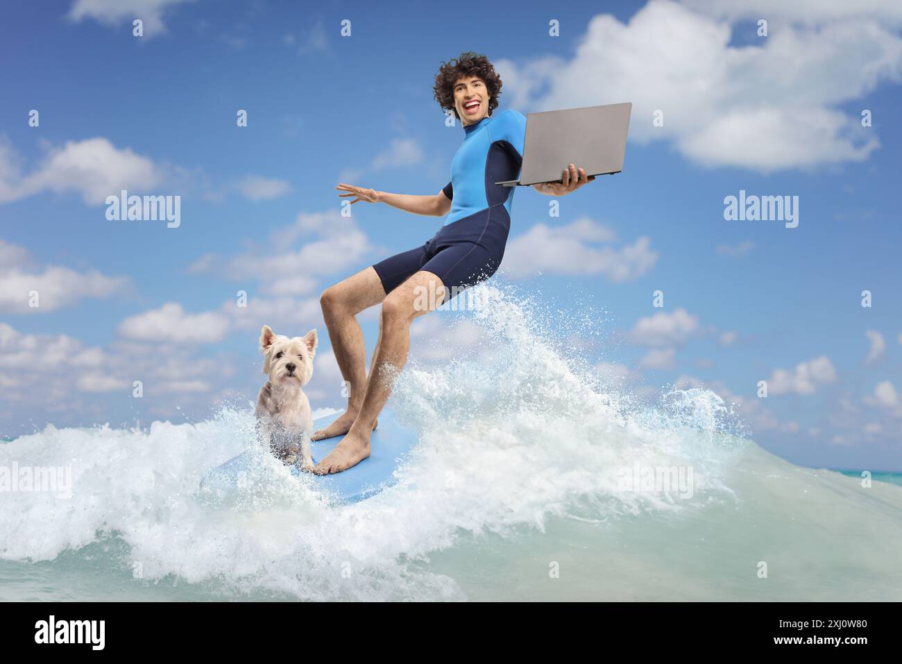 Junger Mann in einem Neoprenanzug mit einem Hund, der auf einem Surfbrett im Meer reitet und einen Laptop benutzt Stockfoto