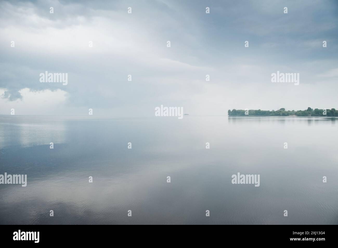 See bei bewölktem Wetter. Ruhiges Wasser direkt vor dem Sturm. Dramatischer Himmel, der sich in der Wasseroberfläche spiegelt. Stockfoto