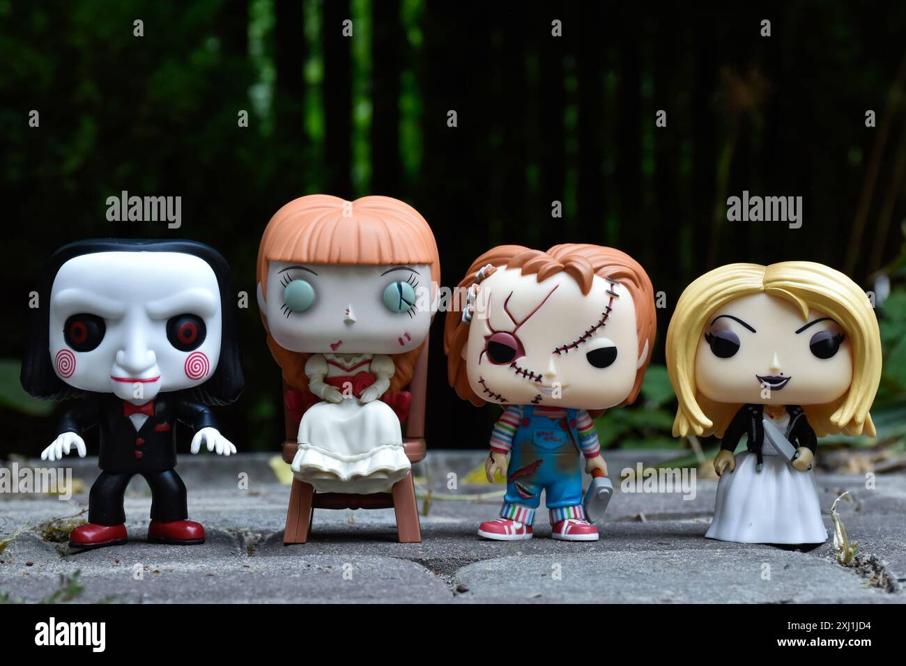 Funko Pop Actionfiguren von bösen Puppen aus Horrorfilmen. Billy die Puppe, Annabelle, Chucky und Tiffany. Dunkler Hof, schwarzer Zaun, stimmungsvolles Grün. Stockfoto