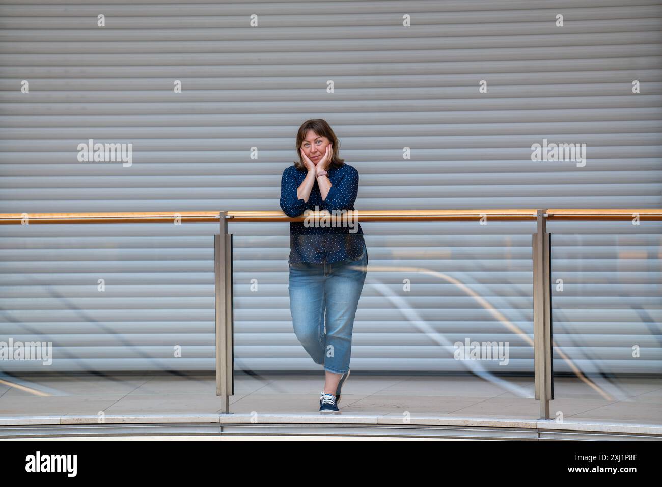 Porträt einer 50-jährigen Frau. Eine Dame steht in einem Einkaufszentrum vor dem Hintergrund geschlossener Jalousien. Stützt den Kopf mit den Händen Stockfoto