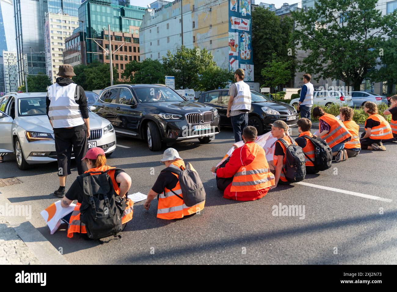 Aktivisten sitzen auf der Straße und blockieren während der Demonstration Autos vor ihnen. Menschen in orangefarbenen Westen (Aktivisten der letzten Generation) blockierten den Verkehr auf Aleja Jana Pawla II. Das sind Aktivisten der letzten Generation, die Investitionen in öffentliche Verkehrsmittel fordern. Die letzte Generation blockiert die Hauptarterien Warschaus seit der dritten Woche. Die letzte Generation erklärte vor den Kameras: Wir halten nicht an, unser Ziel ist die längste Reihe ziviler Widerstandskämpfe gegen den Klimawandel in Polen. In der heißesten Jahreszeit gehen Menschen, die sich der rechtlichen Konsequenzen bewusst sind, auf die Straße. Stockfoto