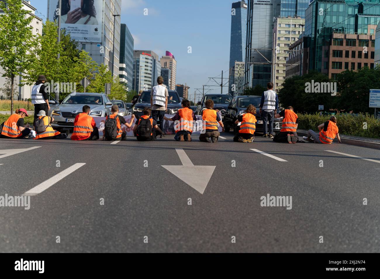 Aktivisten sitzen während der Demonstration auf drei Fahrspuren der Straßensperre. Menschen in orangefarbenen Westen (Aktivisten der letzten Generation) blockierten den Verkehr auf Aleja Jana Pawla II. Das sind Aktivisten der letzten Generation, die Investitionen in öffentliche Verkehrsmittel fordern. Die letzte Generation blockiert die Hauptarterien Warschaus seit der dritten Woche. Die letzte Generation erklärte vor den Kameras: Wir halten nicht an, unser Ziel ist die längste Reihe ziviler Widerstandskämpfe gegen den Klimawandel in Polen. In der heißesten Jahreszeit sind sich die Menschen der rechtlichen Konsequenzen bewusst Stockfoto