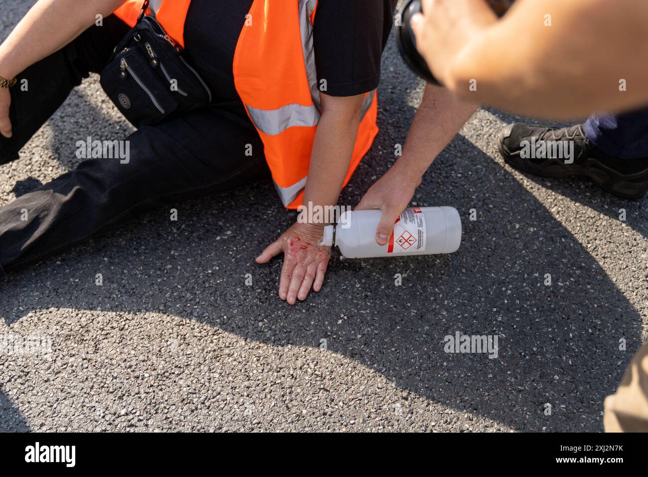 Ein Polizist entfernt die Hand des Aktivisten während der Demonstration vom Asphalt. Menschen in orangefarbenen Westen (Aktivisten der letzten Generation) blockierten den Verkehr auf Aleja Jana Pawla II. Das sind Aktivisten der letzten Generation, die Investitionen in öffentliche Verkehrsmittel fordern. Die letzte Generation blockiert die Hauptarterien Warschaus seit der dritten Woche. Die letzte Generation erklärte vor den Kameras: Wir halten nicht an, unser Ziel ist die längste Reihe ziviler Widerstandskämpfe gegen den Klimawandel in Polen. In der heißesten Jahreszeit sind sich die Menschen der rechtlichen Konsequenzen bewusst Stockfoto