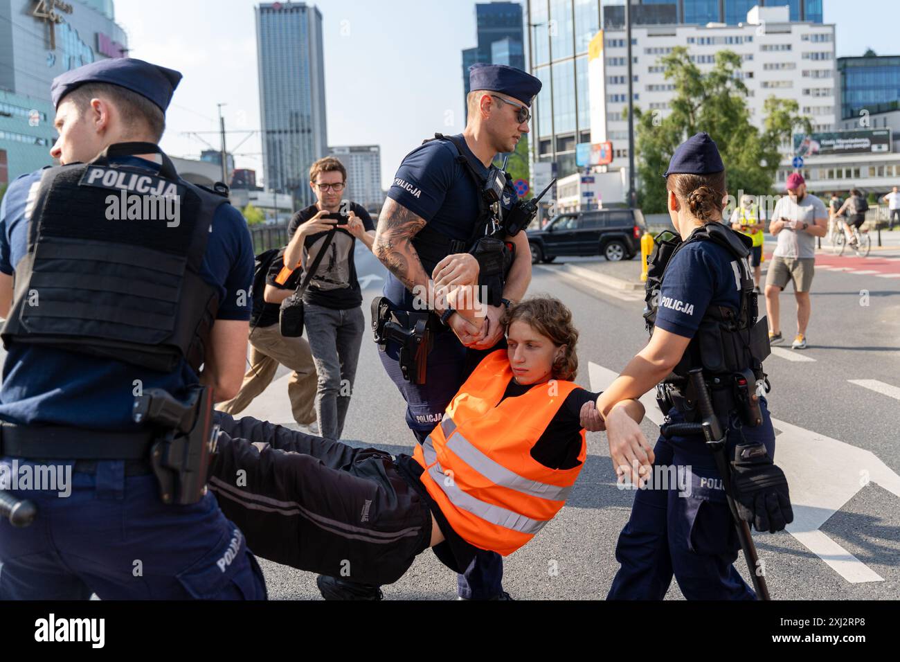 Polizisten tragen während der Demonstration einen Aktivist in einer orangefarbenen Weste von der Straße. Menschen in orangefarbenen Westen (Aktivisten der letzten Generation) blockierten den Verkehr auf Aleja Jana Pawla II. Das sind Aktivisten der letzten Generation, die Investitionen in öffentliche Verkehrsmittel fordern. Die letzte Generation blockiert die Hauptarterien Warschaus seit der dritten Woche. Die letzte Generation erklärte vor den Kameras: Wir halten nicht an, unser Ziel ist die längste Reihe ziviler Widerstandskämpfe gegen den Klimawandel in Polen. In der heißesten Jahreszeit nehmen Menschen, die sich der rechtlichen Konsequenzen bewusst sind, es Stockfoto