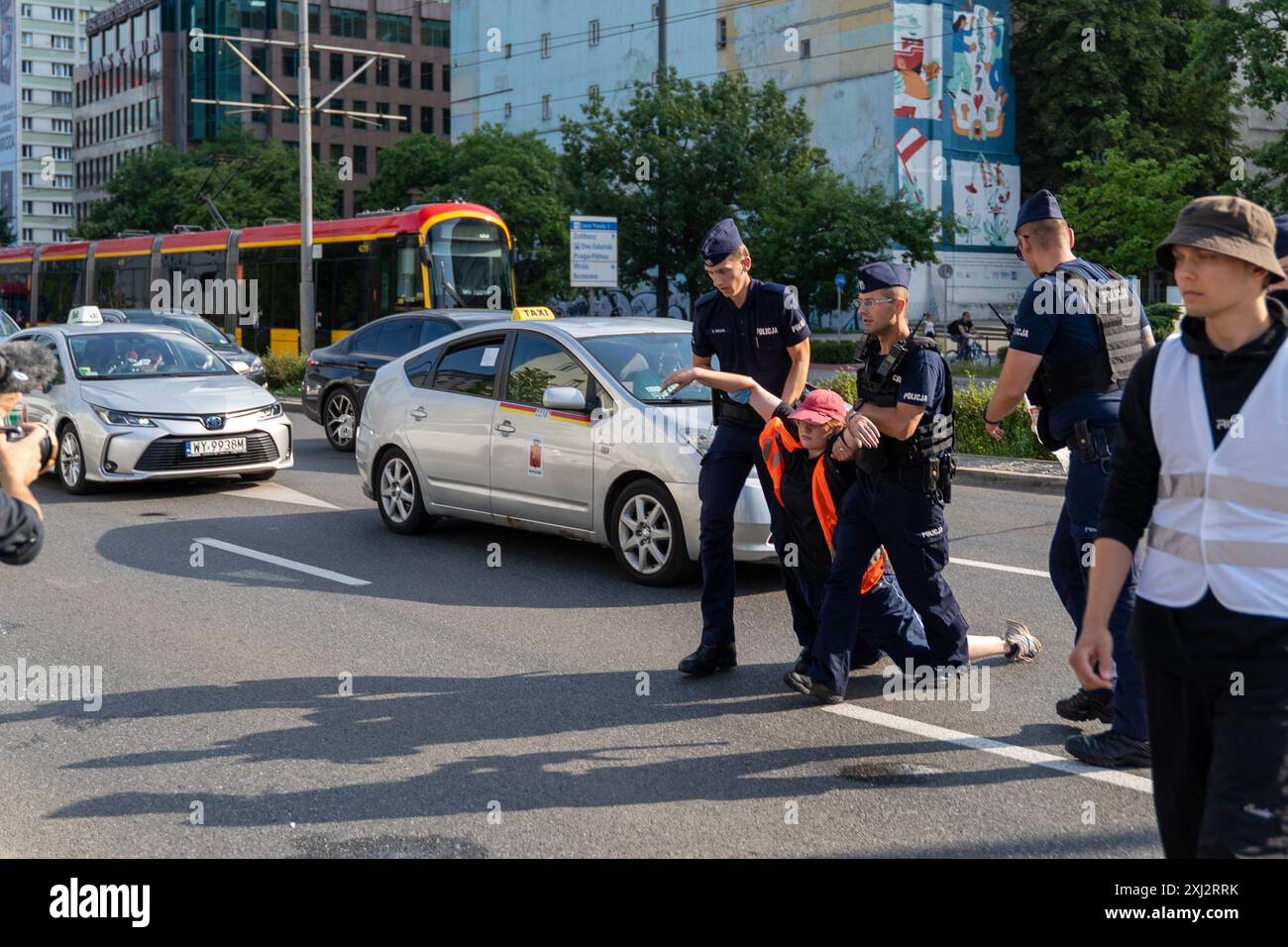 Polizisten tragen während der Demonstration einen Aktivist in einer orangefarbenen Weste von der Straße. Menschen in orangefarbenen Westen (Aktivisten der letzten Generation) blockierten den Verkehr auf Aleja Jana Pawla II. Das sind Aktivisten der letzten Generation, die Investitionen in öffentliche Verkehrsmittel fordern. Die letzte Generation blockiert die Hauptarterien Warschaus seit der dritten Woche. Die letzte Generation erklärte vor den Kameras: Wir halten nicht an, unser Ziel ist die längste Reihe ziviler Widerstandskämpfe gegen den Klimawandel in Polen. In der heißesten Jahreszeit nehmen Menschen, die sich der rechtlichen Konsequenzen bewusst sind, es Stockfoto