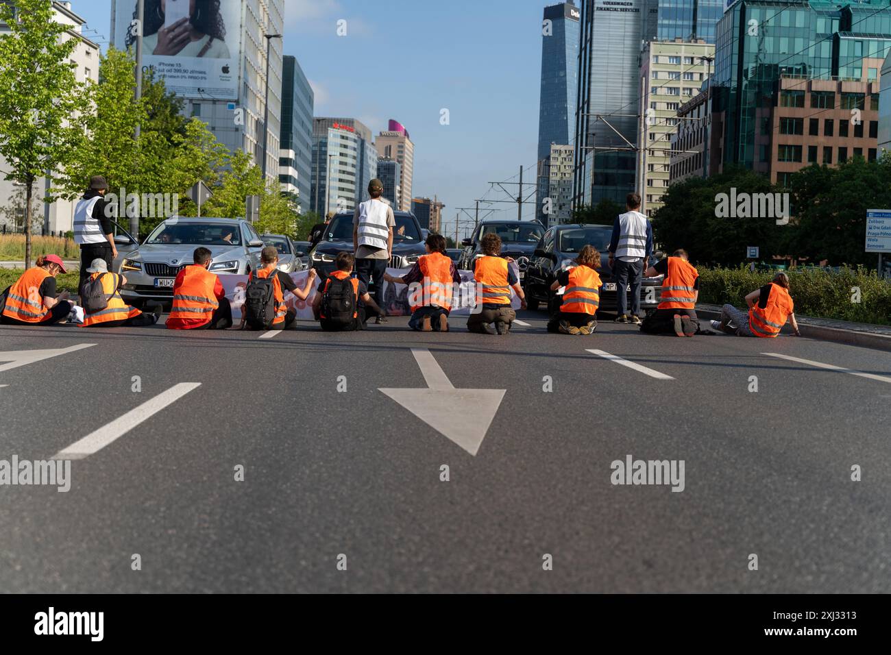15. Juli 2024, Warschau, Polen: Aktivisten sitzen während der Demonstration auf drei Fahrspuren der Straßensperre. Menschen in orangefarbenen Westen (Aktivisten der letzten Generation) blockierten den Verkehr auf Aleja Jana Pawla II. Das sind Aktivisten der letzten Generation, die Investitionen in öffentliche Verkehrsmittel fordern. Die letzte Generation blockiert die Hauptarterien Warschaus seit der dritten Woche. Die letzte Generation erklärte vor den Kameras: Wir halten nicht an, unser Ziel ist die längste Reihe ziviler Widerstandskämpfe gegen den Klimawandel in Polen. In der heißesten Jahreszeit, wissen die Leute von der lega Stockfoto