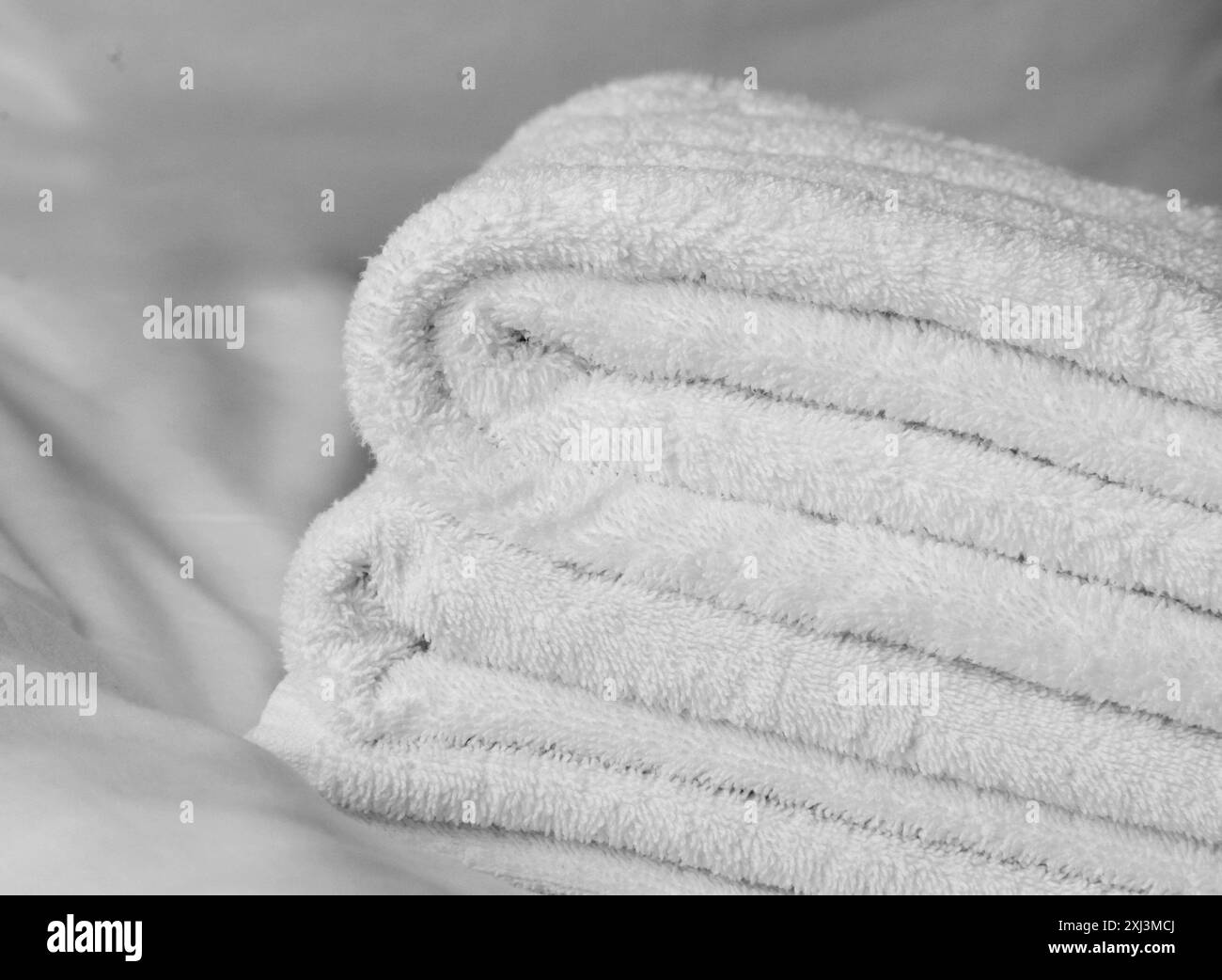 Gefaltete weiße Handtücher liegen auf einem weißen Laken. Stockfoto