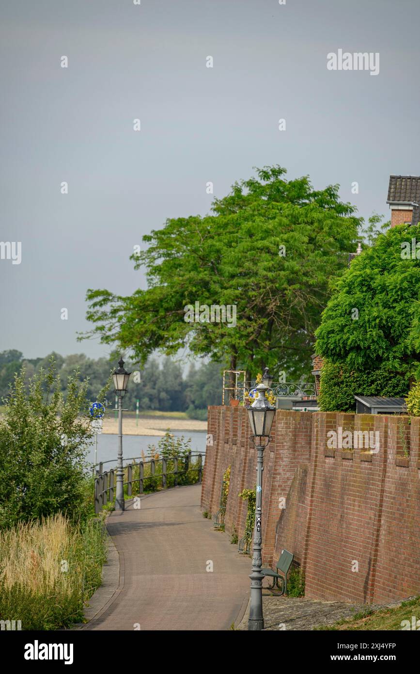 Friedlicher kleiner Pfad entlang einer Backsteinmauer mit Blick auf den Fluss und umgeben von grünen Bäumen, rees, deutschland Stockfoto