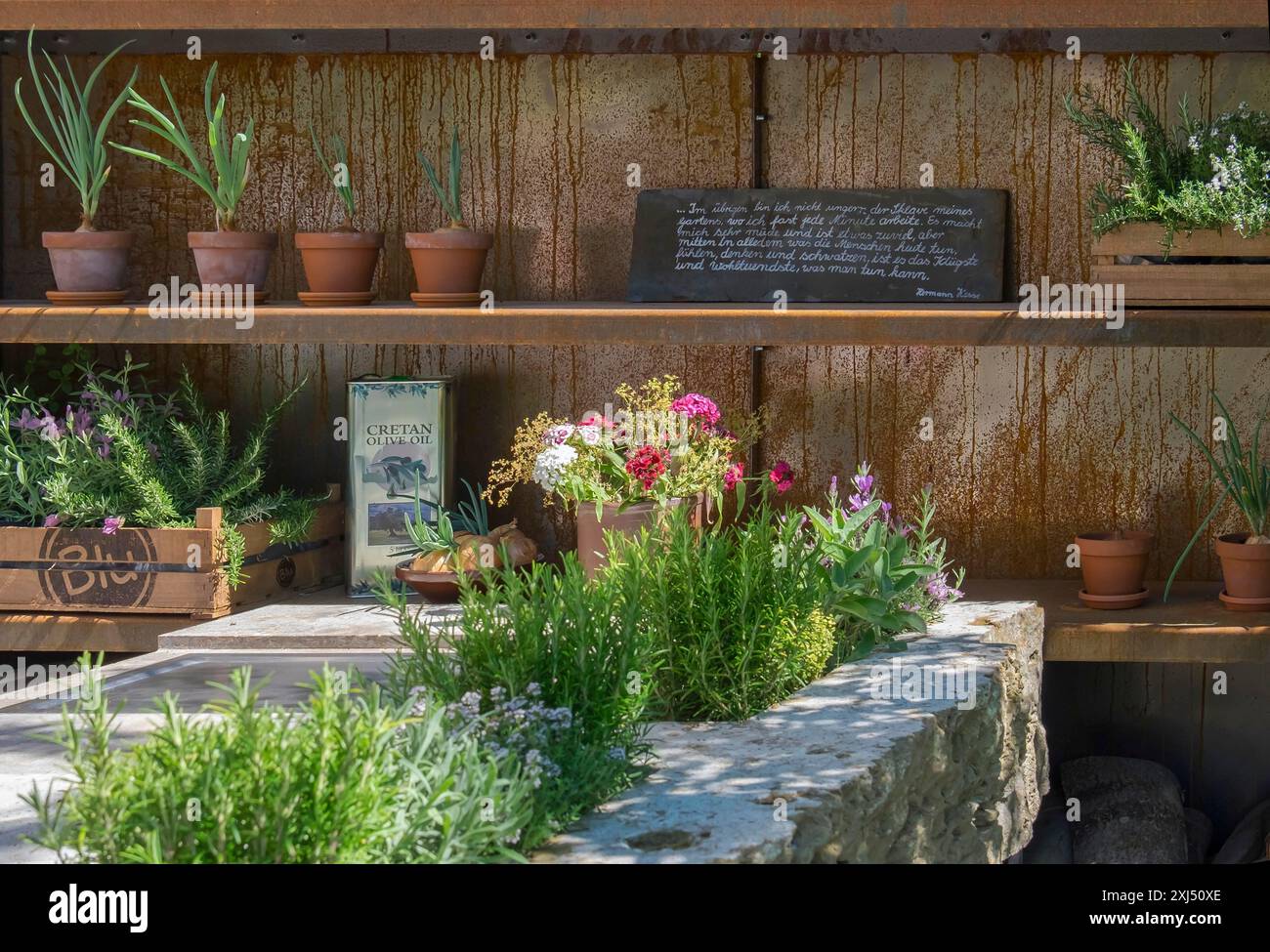 Rustikales Holzregal mit Tontöpfen und verschiedenen Pflanzen, ein Steintisch mit Kräutern und eine Tafel im Hintergrund, Landesgartenschau Bad Stockfoto