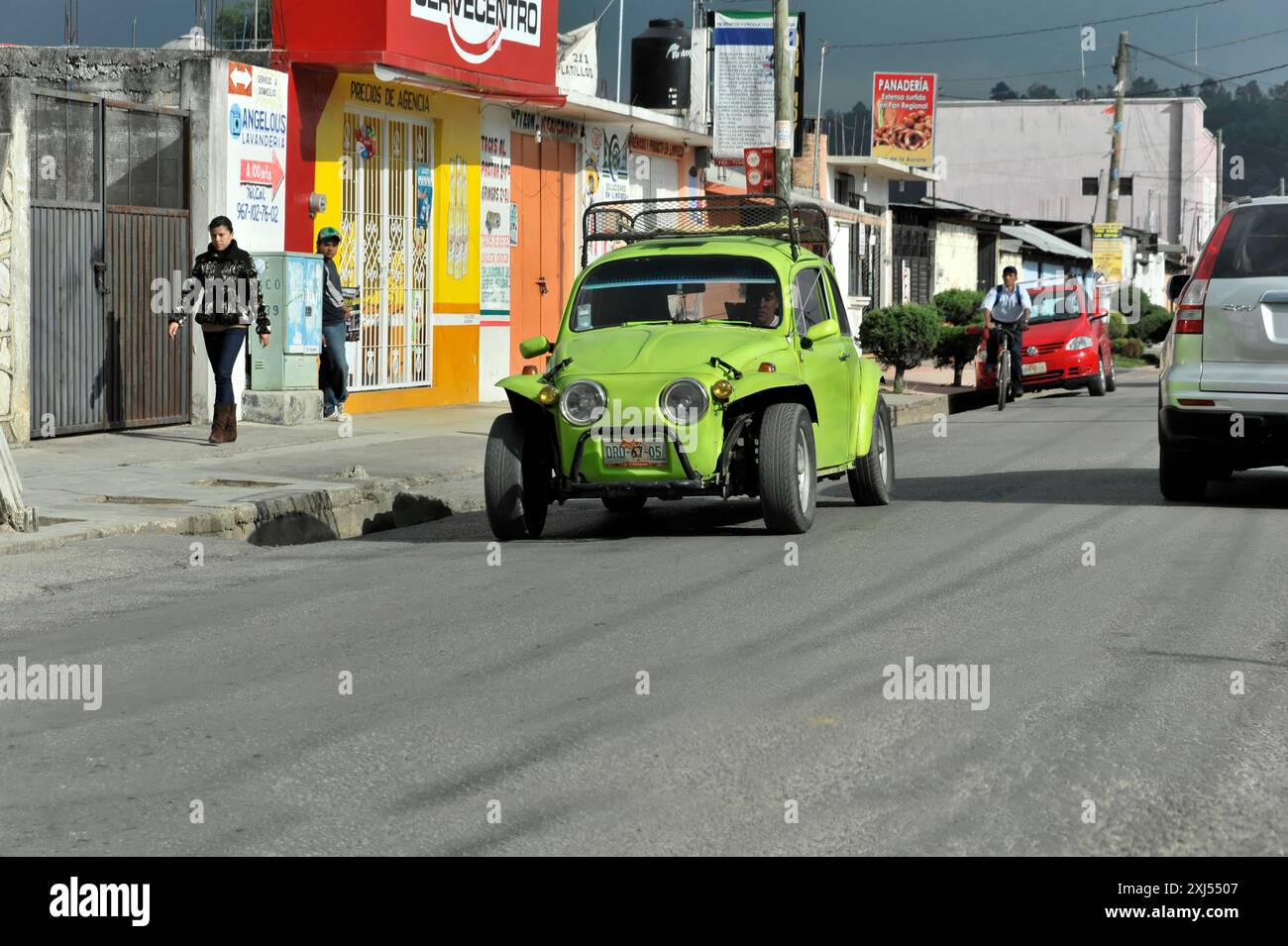 San Christobal de las Casas, Mexiko, Mittelamerika, grünes Auto, das auf einer Straße in einer städtischen Umgebung fährt. Leute, die auf dem Bürgersteig laufen, einkaufen Stockfoto