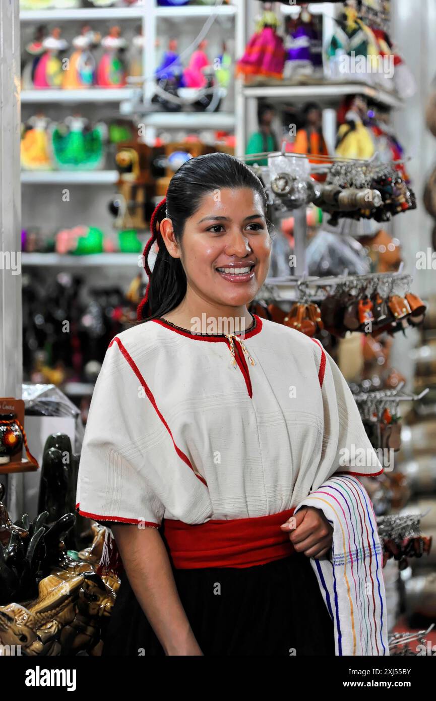 Oaxaca, Mexiko, Mittelamerika, lächelnde Frau in traditioneller Kleidung vor einem Verkaufsstand, in dem buntes Kunsthandwerk und Schmuck verkauft werden Stockfoto