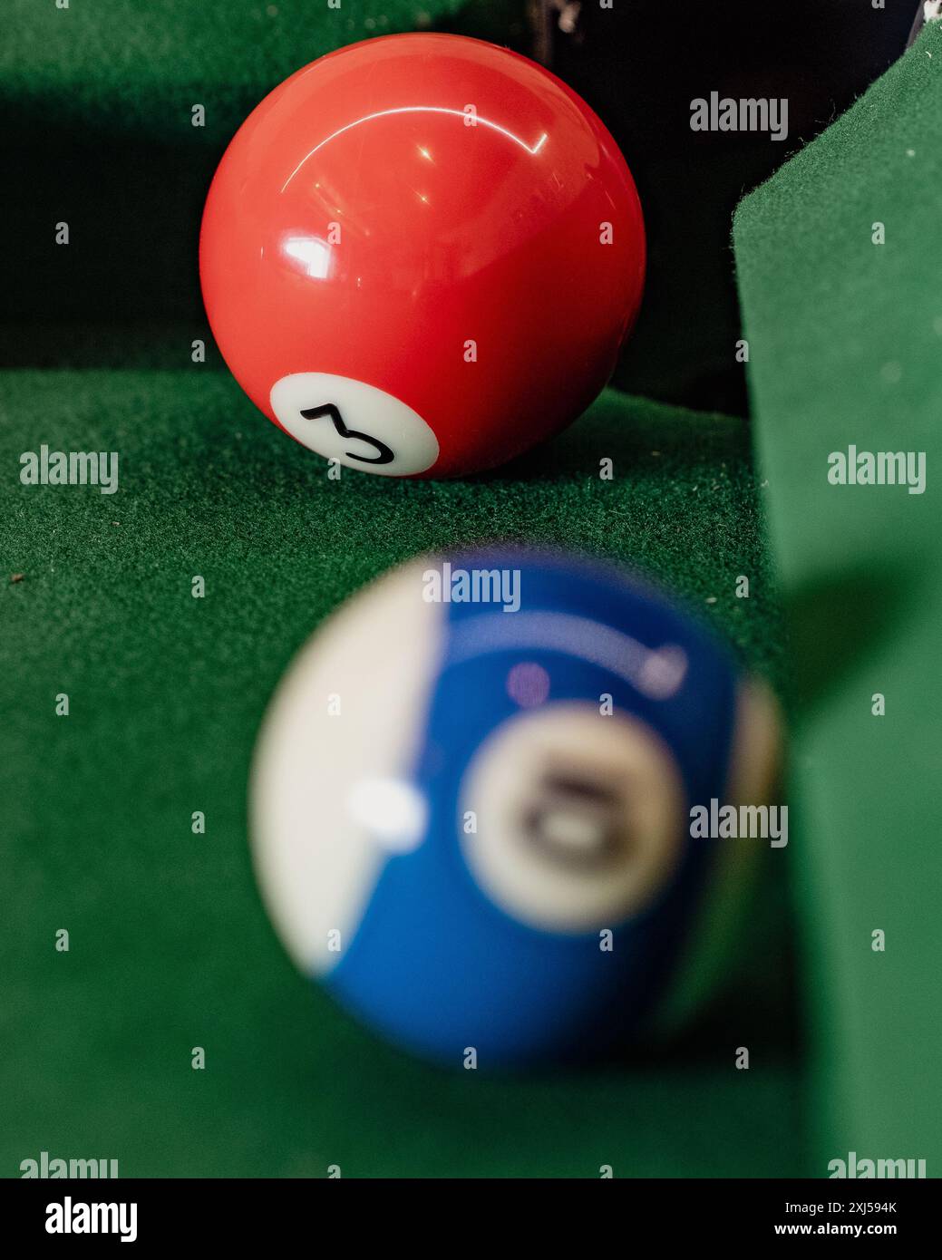 Makroaufnahme einer Billardanlage mit Fokus auf die rot und blau gestreiften Poolbälle vor dem üppig grünen Hintergrund, die Präzision und Strategie veranschaulichen Stockfoto