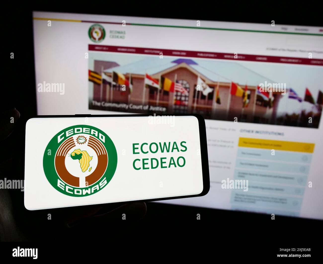 Stuttgart, Deutschland, 15.02.2024: Person, die ein Mobiltelefon mit dem Logo der Wirtschaftsgemeinschaft westafrikanischer Staaten (ECOWAS) vor der Webseite hält. Stockfoto