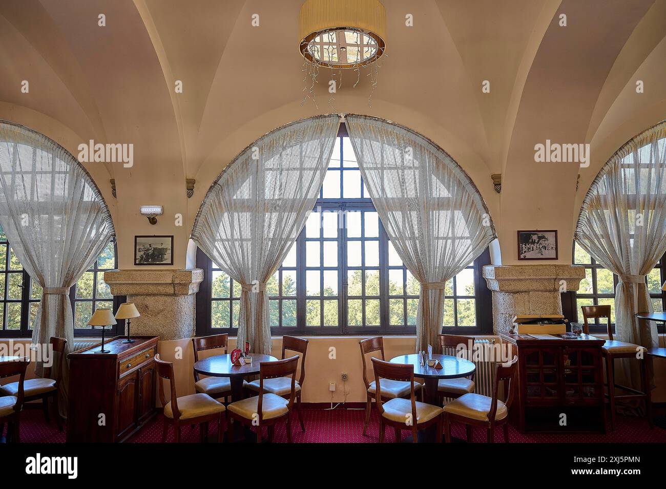 Ein helles Café mit großen Bogenfenstern, Holzmöbeln und roten Teppichen, das eine warme, einladende Atmosphäre ausstrahlt, das Elafos Hotel, Profitis Ilias Stockfoto