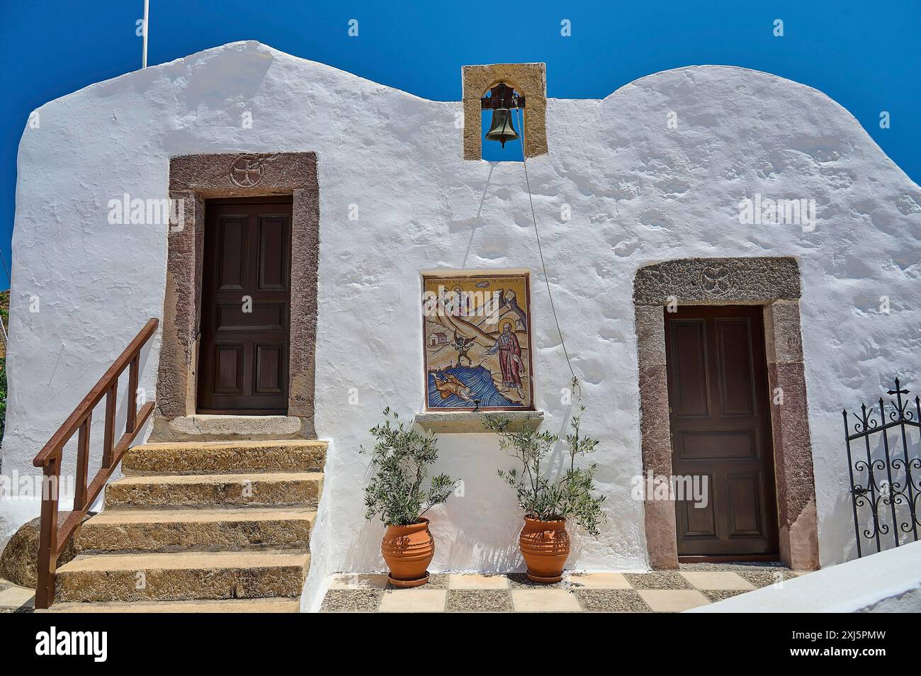 Traditionelles griechisches Gebäude mit weißer Wand, zwei Türen, Glocke und Treppe unter blauem Himmel, Baptisterium, St. Johannes der Theologe, Skala, Patmos Stockfoto