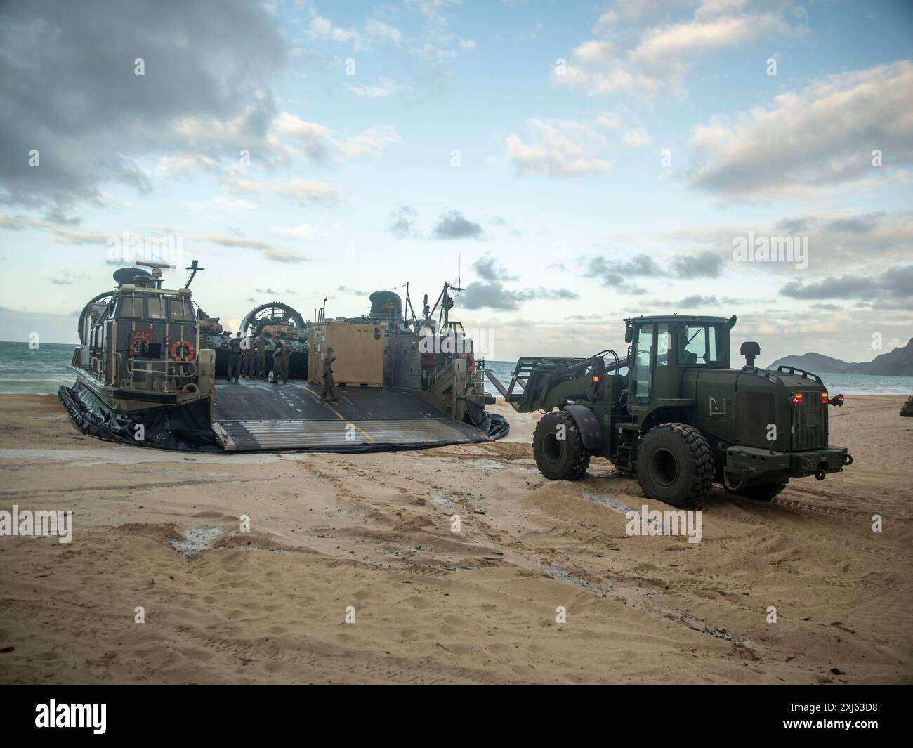 Ein Traktor des U.S. Marine Corps 624-KR, gummimüde, knickgelenkte Lenkung, Mehrzweckfahrzeug, das dem Combat Logistics Battalion 15, 15. Marine Expeditionary Unit, zugeteilt ist, nähert sich einem Landeboot, Luftkissen, um einen Container im Marine Corps Training Area Bellows, Waimanalo, Hawaii, zu entladen. während einer LCAC-Entladung während der Teilnahme an Übung Rim of the Pacific 2024, 14. Juli. 29 Nationen, 40 Überlandschiffe, drei U-Boote, 14 nationale Landstreitkräfte, mehr als 150 Flugzeuge und 25.000 Mitarbeiter nehmen vom 27. Juni bis 1. August auf den hawaiianischen Inseln Teil. Das weltweit größte internationale Stockfoto