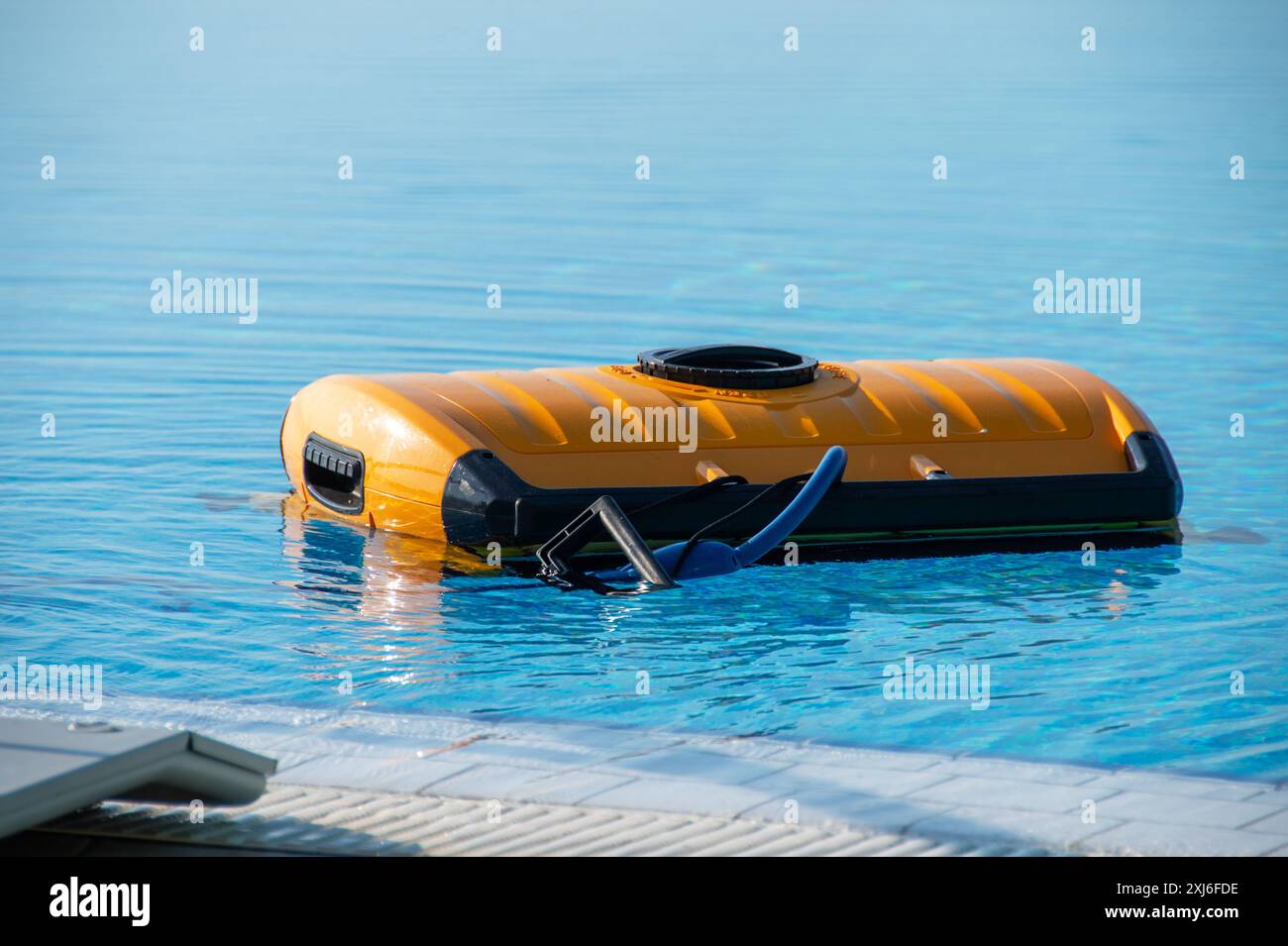 Ein hochmoderner automatisierter Poolreiniger schwimmt auf der Oberfläche eines klar blauen Schwimmbades und spiegelt die neueste Technik der Wartung von Heimbädern wider Stockfoto