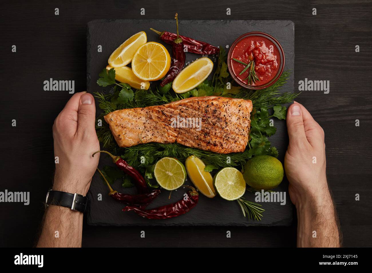 Teilweise mit Blick auf die männliche Hände, gegrilltes Lachssteak, Sauce und Zitrusfrüchte auf schwarze Oberfläche Stockfoto