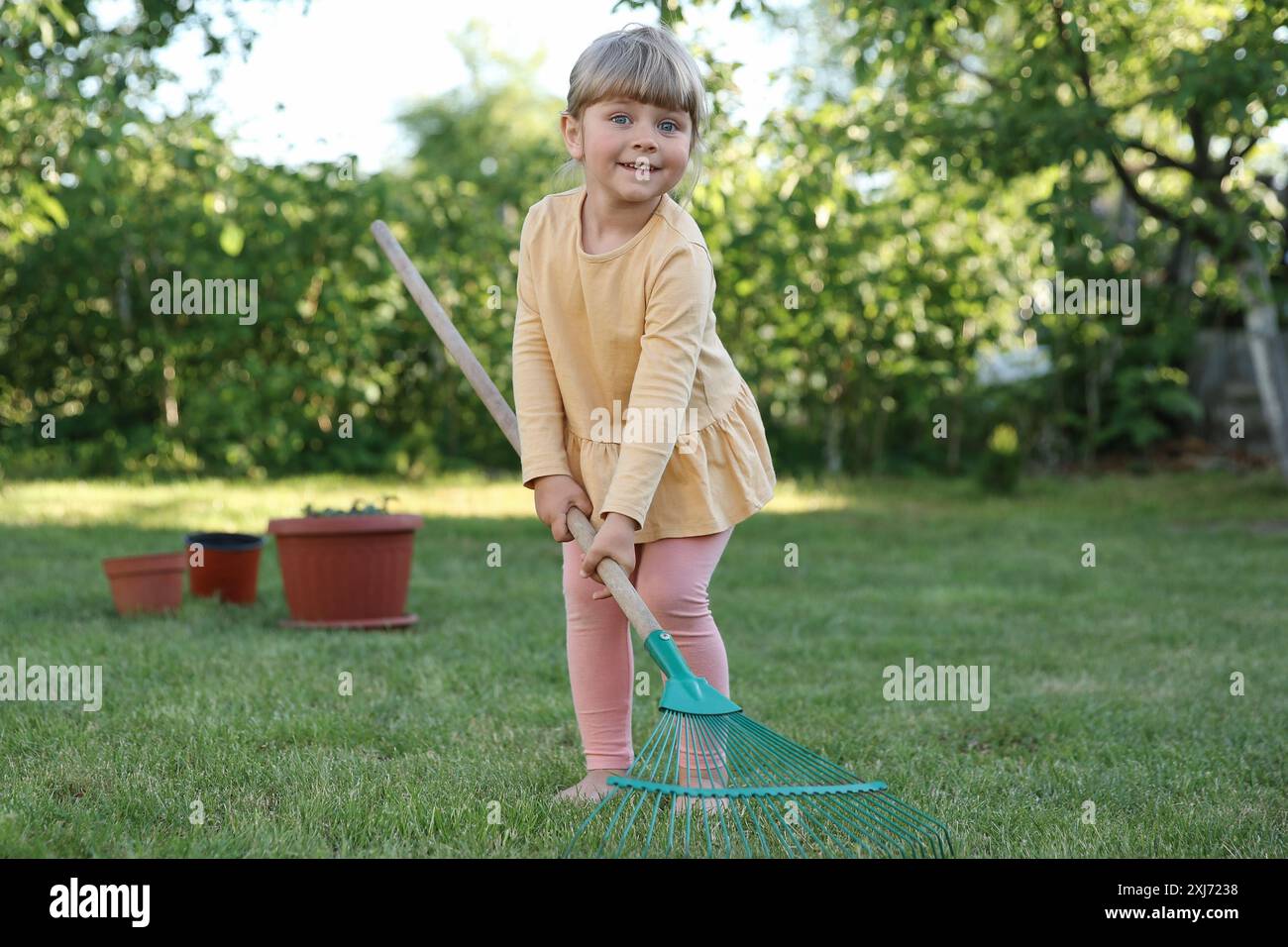 Süßes kleines Mädchen mit Rechen im Garten am Frühlingstag Stockfoto