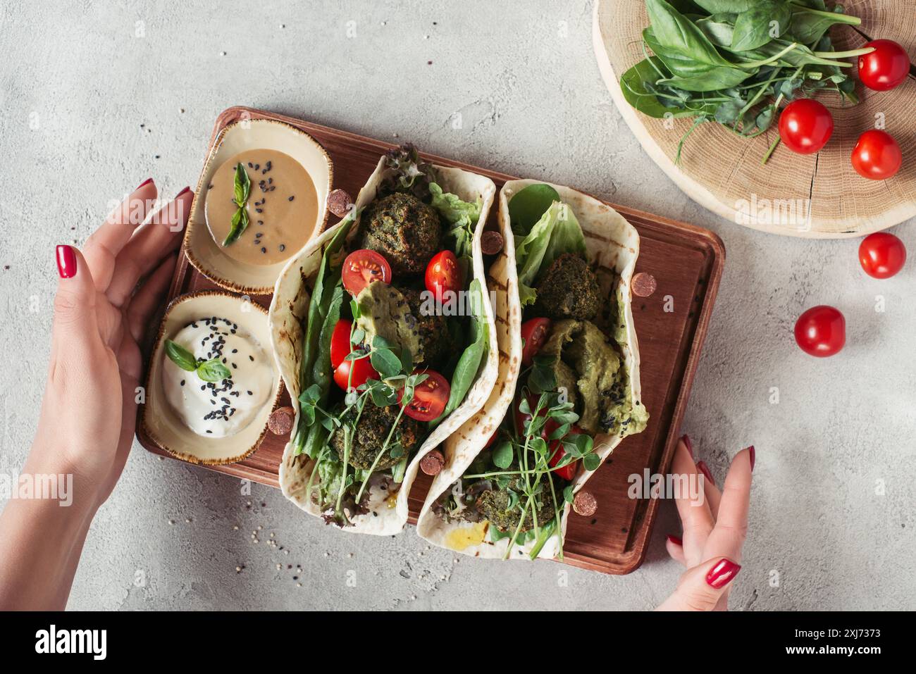 Frau, die Falafel mit Tortillas, Kirschtomaten und gekeimten Sonnenblumenkernen hält Stockfoto