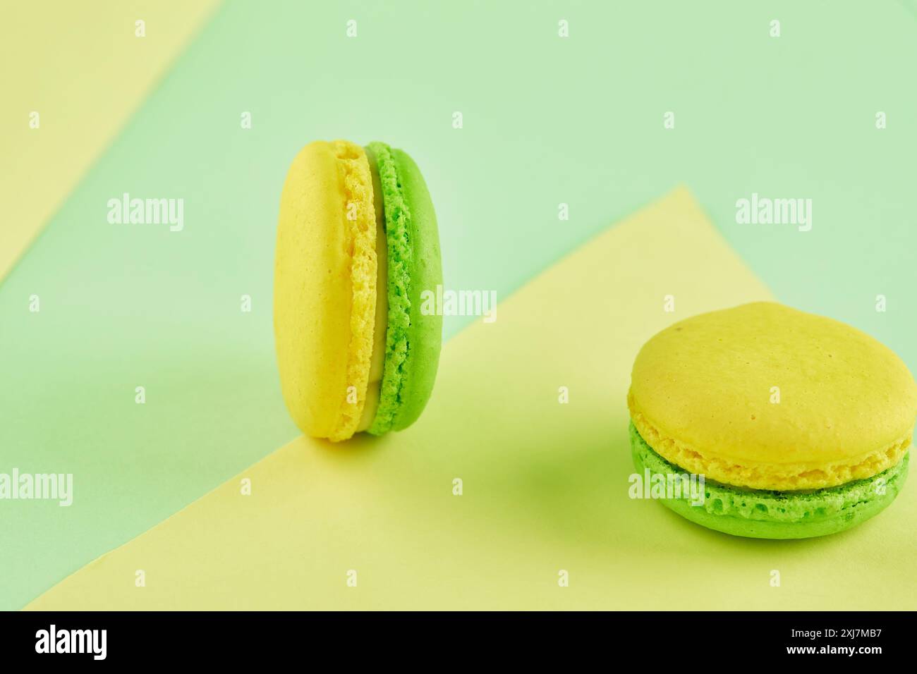 Grüne und gelbe Macarons gepaart mit Limettenkeilen und weißer Schokolade, neben einer Margarita mit gesalzenem Rand. Stockfoto