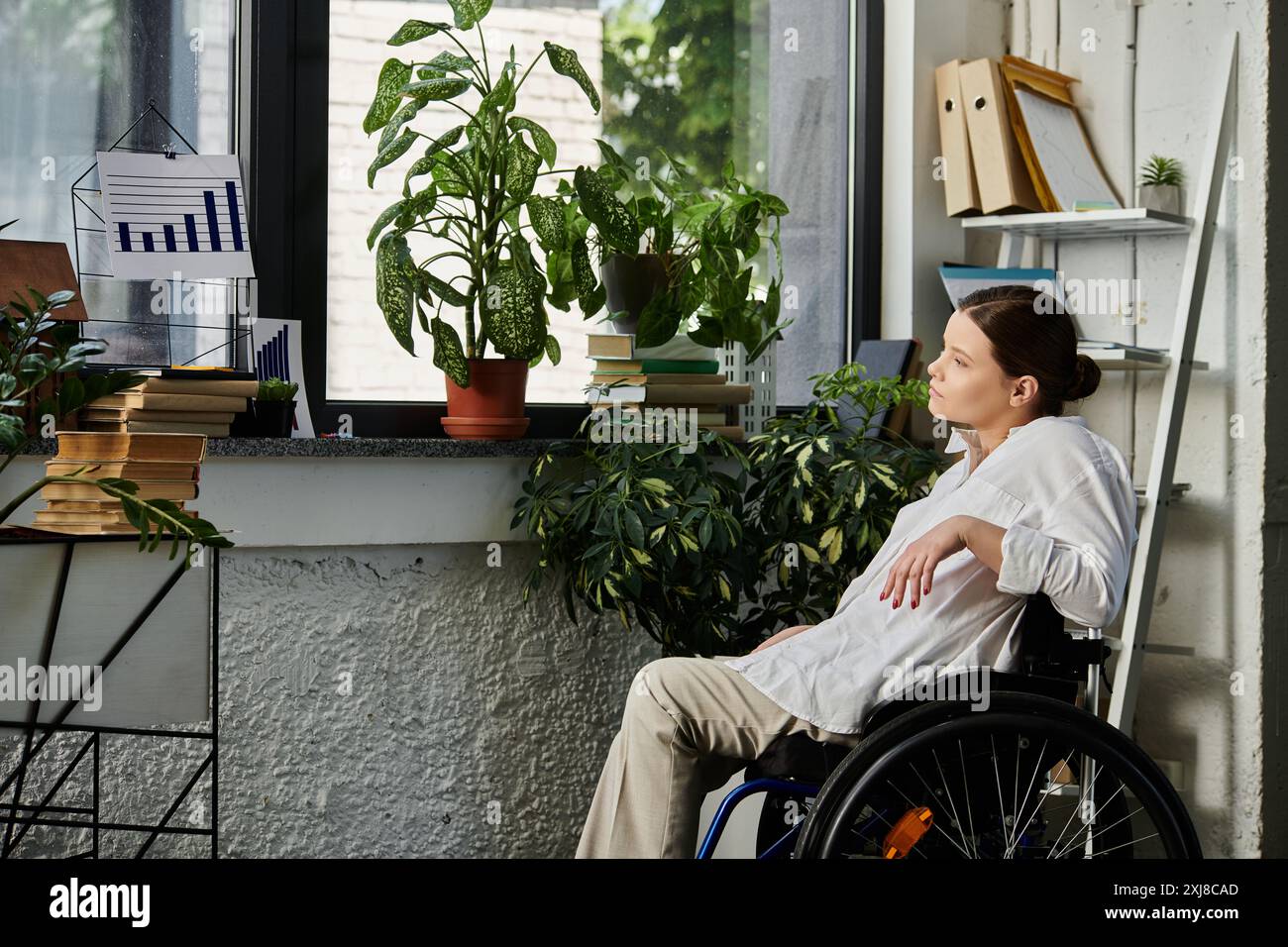 Eine junge Geschäftsfrau im Rollstuhl arbeitet in einem modernen Büro mit Tageslicht und Pflanzen. Stockfoto