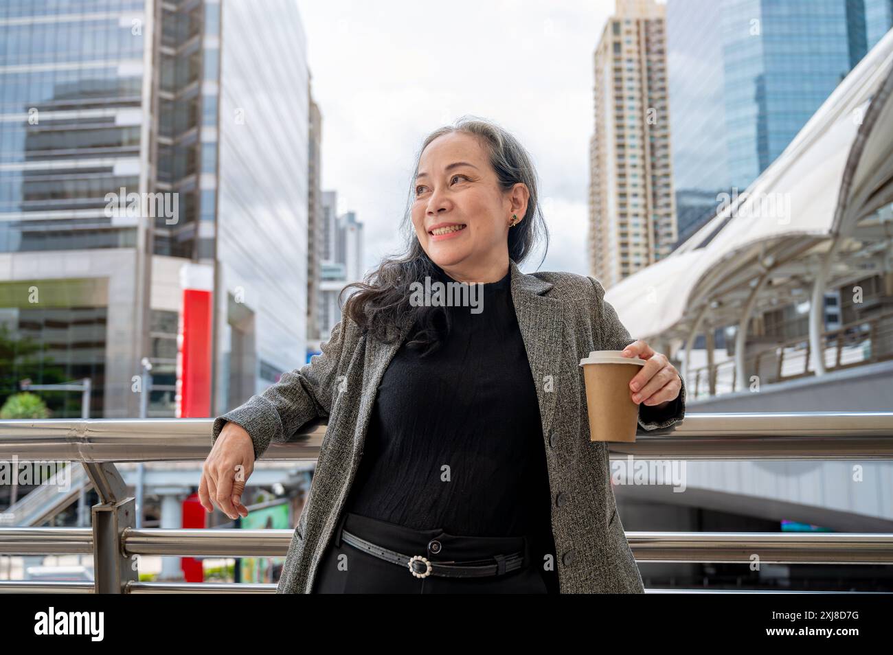 Eine selbstbewusste, positive, reife asiatische Geschäftsfrau steht auf einem Wolkenkratzer in der belebten Stadt. Stockfoto