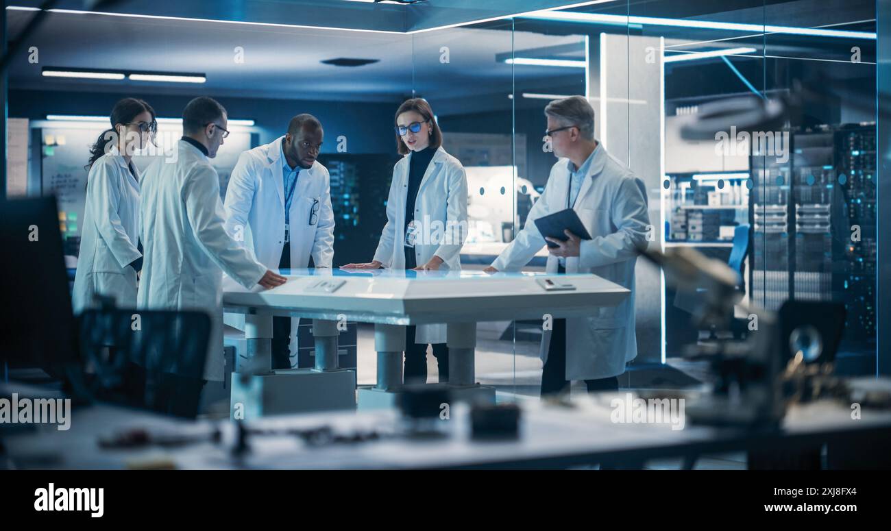 Ingenieure, Wissenschaftler und Entwickler versammelten sich am beleuchteten Konferenztisch im Technology Research Center, um zu sprechen, Lösungen zu finden und industrielle Lösungen für moderne Fabriken zu analysieren. Stockfoto