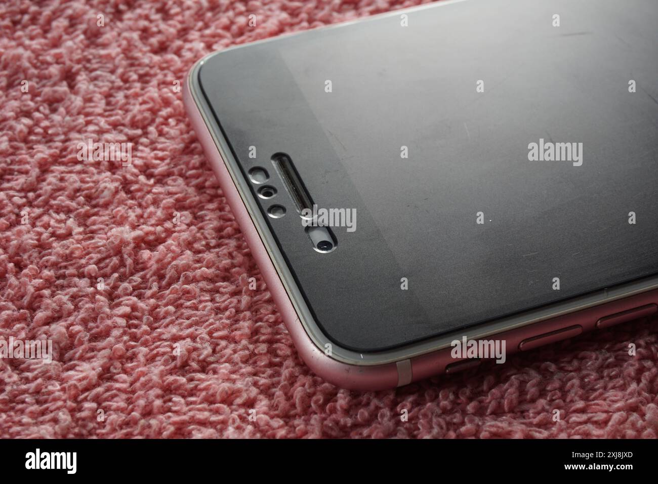 Nahaufnahme des Apple iphone Sensors, der vorderen Kamera und des vorderen Lautsprechers auf rotem Hintergrund. Pink Apple iphone-Gerät. Stockfoto