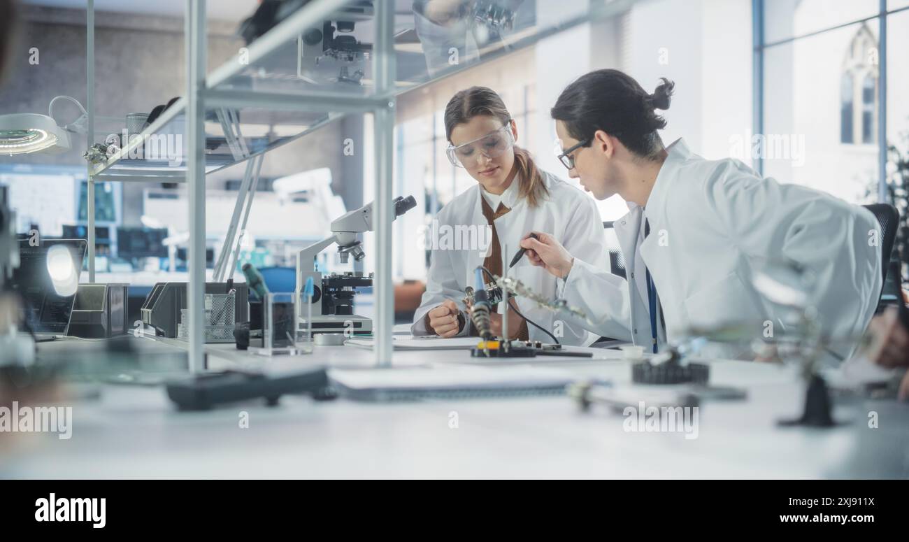 Weibliche und männliche Studenten in Schutzbrillen und weißen Mänteln arbeiten zusammen im Wissenschaftsunterricht, an einem College-Projekt. Wissenschaftler sprechen, studieren und bereiten sich auf Computeringenieurprüfungen vor Stockfoto
